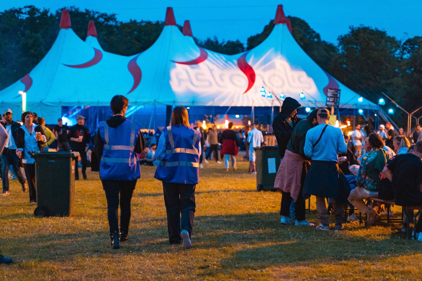 Deux personnes de l'équipe en maraude, de dos, traversent le festival vers le chapiteau principal.