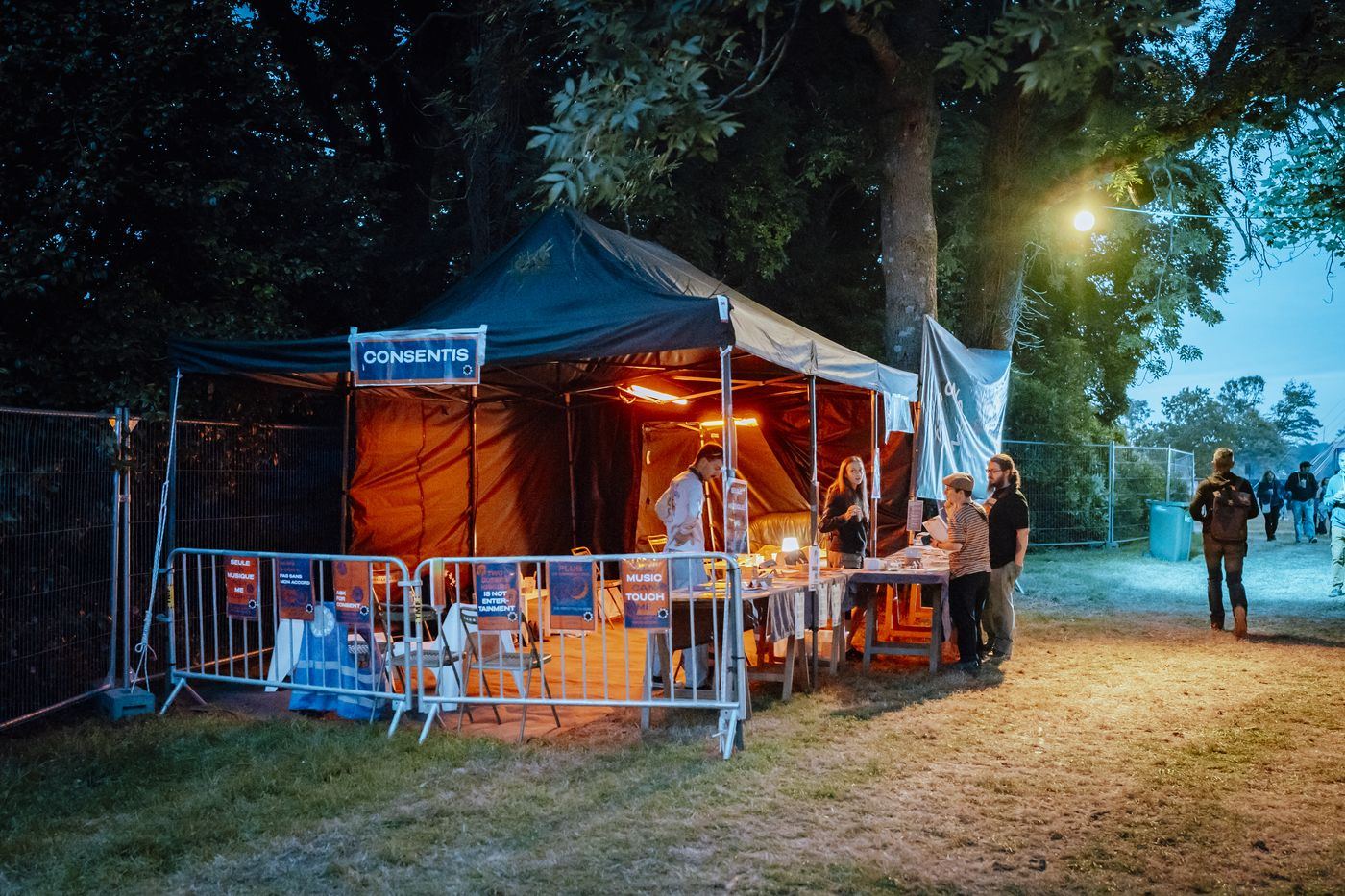 Le stand Consentis éclairé à la tombée de la nuit, sous chapiteau, dans une allée de festival.