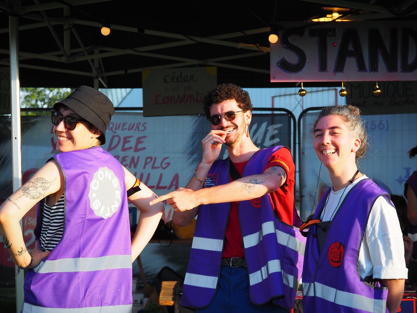 Trois bénévoles en gilet violet Consentis devant le stand, en train de rire.